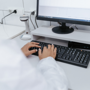 Female pharmacist in white coat utilizing medication management software system on her work computer.