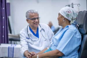 Woman wearing a head scarf is recovering in oncology unit of a hospital, and is sitting alongside her male doctor as he provides support
